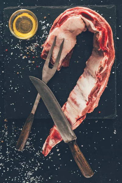 Top view of raw pork ribs slice with cutlery and oil on stone slate — Stock Photo
