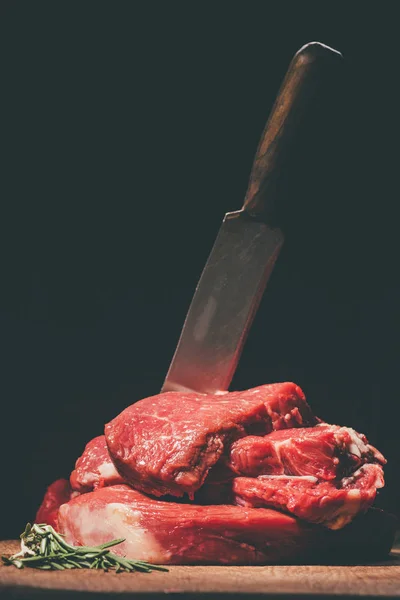 Heap of raw steaks with knife on wooden board — Stock Photo