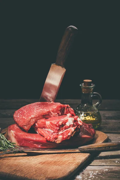 Bifes crus com talheres e especiarias em tábua de corte de madeira em preto — Stock Photo