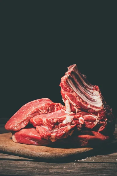 Várias carnes cruas em tábua de corte de madeira em preto — Fotografia de Stock