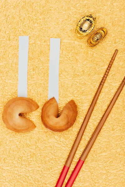 Vista dall'alto dei biscotti cinesi della fortuna con bacchette e lingotti d'oro sulla superficie dorata, concetto di Capodanno cinese — Foto stock