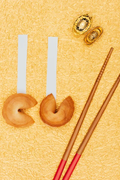 Top view of chinese fortune cookies with chopsticks and gold ingots on golden surface, Chinese New Year concept — Stock Photo