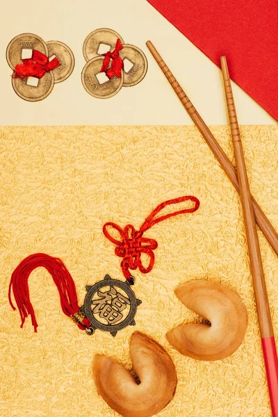 Vista superior de talismanes chinos con galletas de la fortuna y palillos en la superficie dorada, concepto de año nuevo chino - foto de stock