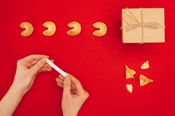 Tiro recortado de mulher abrindo biscoito da sorte sobre a superfície vermelha com caixa de presente artesanal, conceito de Ano Novo Chinês — Fotografia de Stock