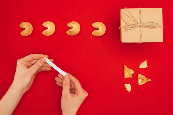 Abgeschnittene Aufnahme einer Frau, die Glückskeks über roter Oberfläche mit handgefertigter Geschenkschachtel öffnet, chinesisches Neujahrskonzept — Stockfoto