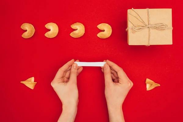 Tiro recortado de la mujer que abre la galleta de la fortuna sobre la superficie roja, concepto de Año Nuevo chino - foto de stock