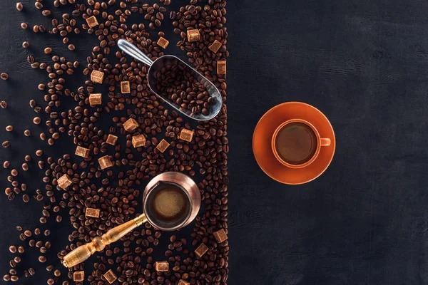 Vista superior de la taza de café con platillo, granos de café tostados, azúcar morena, cafetera y cucharada en negro - foto de stock
