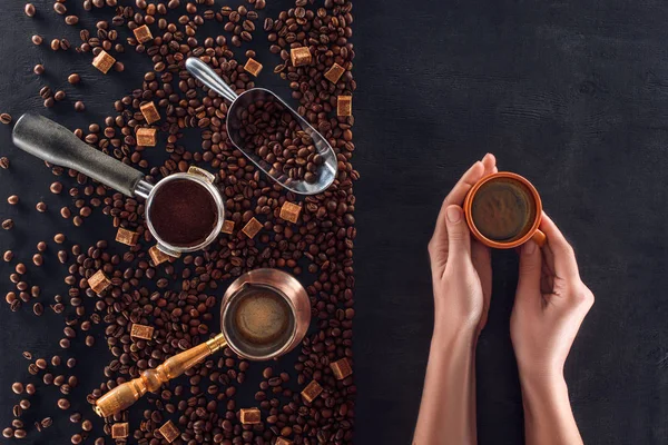 Top view of person holding cup of coffee and roasted coffee beans with coffee pot, scoop and sugar — Stock Photo