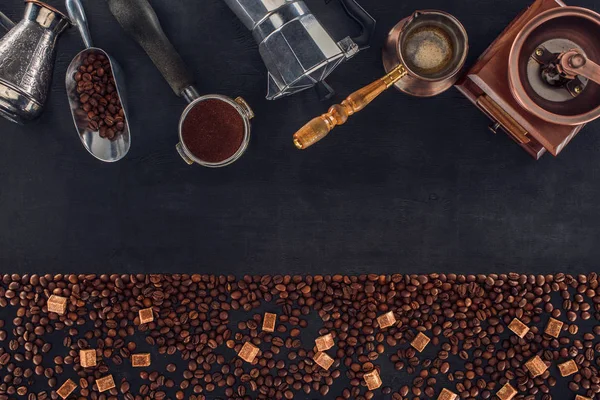 Vista superior de grãos de café torrados com açúcar mascavo e várias cafeteiras e moedores em preto — Fotografia de Stock