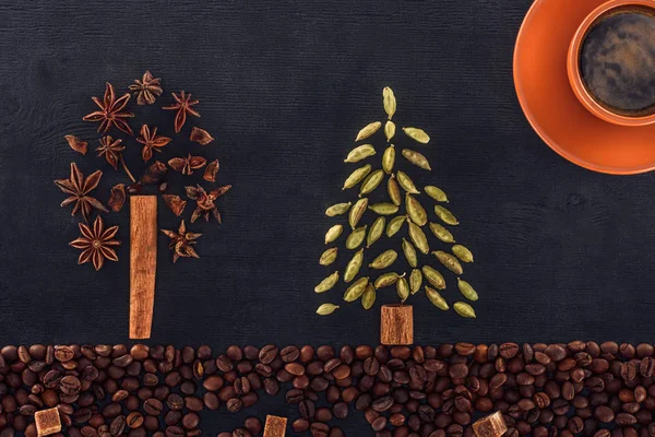 Top view of roasted coffee beans with sugar, cup of coffee and trees symbols made from spices on black — Stock Photo