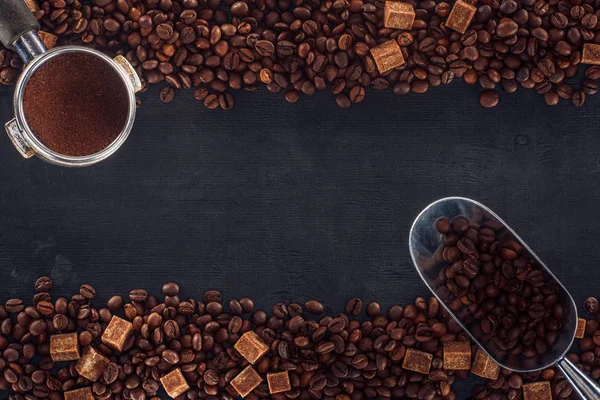 Vista dall'alto di chicchi di caffè torrefatto con zucchero di canna, manomissione di caffè e misurino su nero — Foto stock