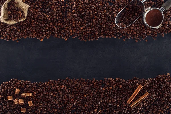Vista superior de granos de café tostados, saco, manipulador de café y cucharada. azúcar morena y palitos de canela en negro - foto de stock