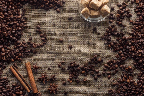 Chicchi di caffè torrefatto con bastoncini di cannella, anice stellato e zucchero di canna in ciotola di vetro su sacco — Foto stock