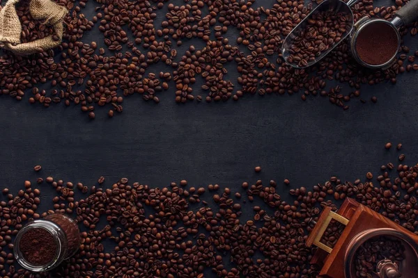 Vue de dessus des grains de café torréfiés, sac, moulin à café et scoop sur noir — Photo de stock