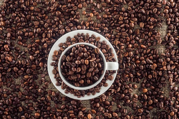 Blick von oben auf Kaffeetasse und geröstete Kaffeebohnen auf Sackkleidung — Stockfoto