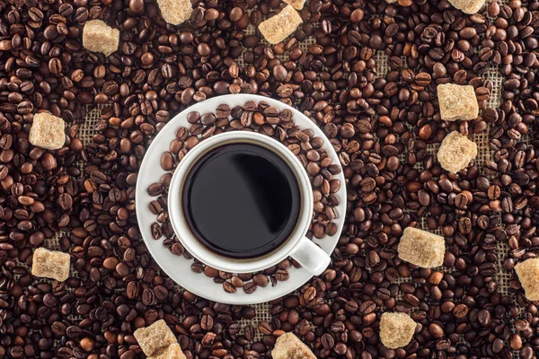 Vista superior de la taza de café con platillo, granos de café tostados y azúcar morena en el saco - foto de stock