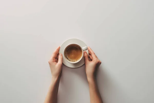 Vista superior de las manos femeninas y taza de café con platillo en gris — Stock Photo