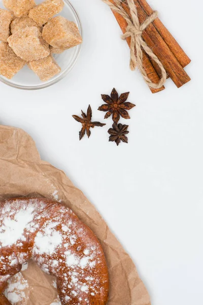 Draufsicht auf frisches Gebäck auf Backpapier, brauner Zucker in Glasschüssel, Sternanis und Zimtstangen mit Seil auf weißem Papier gebunden — Stockfoto