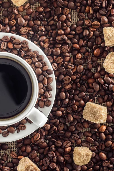 Vista ravvicinata di tazza di caffè, chicchi di caffè torrefatto e zucchero di canna su sacco — Foto stock