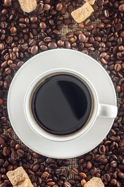 Vue du dessus de tasse de café, grains de café torréfiés et sucre brun sur sac — Photo de stock