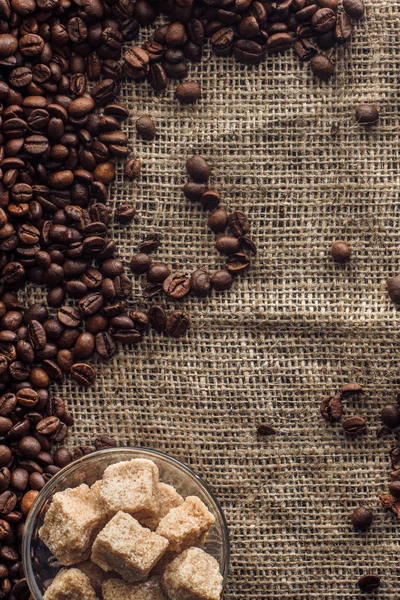 Vue du dessus des grains de café torréfiés avec sucre brun dans un bol en verre sur un sac — Photo de stock