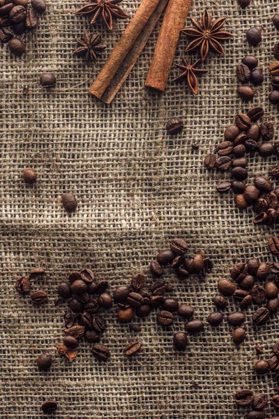 Top view of roasted coffee beans with cinnamon sticks and star anise on sackcloth — Stock Photo