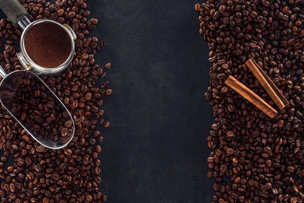 Vue de dessus des grains de café torréfiés avec bâtonnets de cannelle, tampon de café et scoop sur noir — Photo de stock