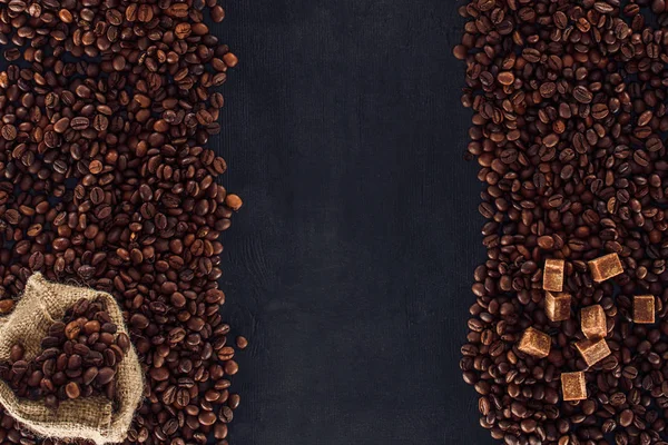 Top view of roasted coffee beans with brown sugar and sackcloth on black — Stock Photo