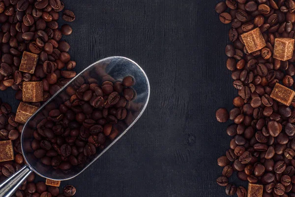 Draufsicht auf geröstete Kaffeebohnen mit braunem Zucker und Schaufel auf schwarz — Stockfoto