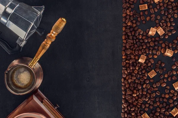 Vue de dessus des grains de café torréfiés avec sucre, cafetière, cafetière et broyeur sur noir — Photo de stock