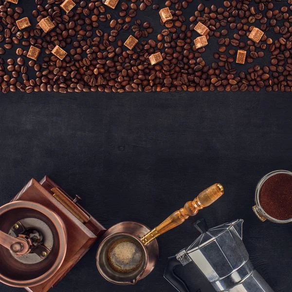 Vista superior de granos de café tostados, cucharada, molinillo de café, cafetera y cafetera en negro - foto de stock