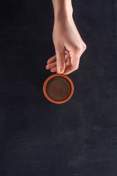 Foto recortada de la mujer sosteniendo la taza de café caliente en la mesa oscura - foto de stock