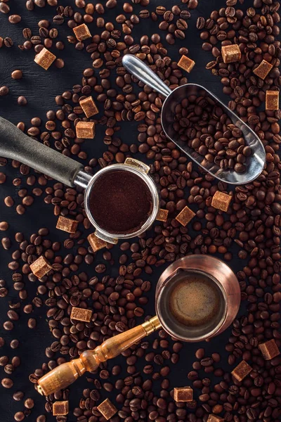 Vue de dessus des grains de café torréfiés, cuillère, tampon de café, cafetière et cassonade sur noir — Photo de stock