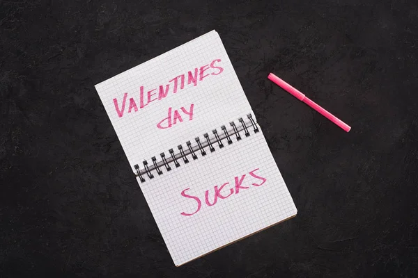 Top view of notebook with valentines day sucks and pen on dark tabletop — Stock Photo