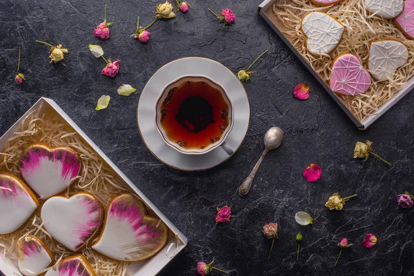 St dia dos namorados flat lay com xícara de chá, biscoitos em forma de coração envidraçado e flores decorativas em mesa escura — Fotografia de Stock