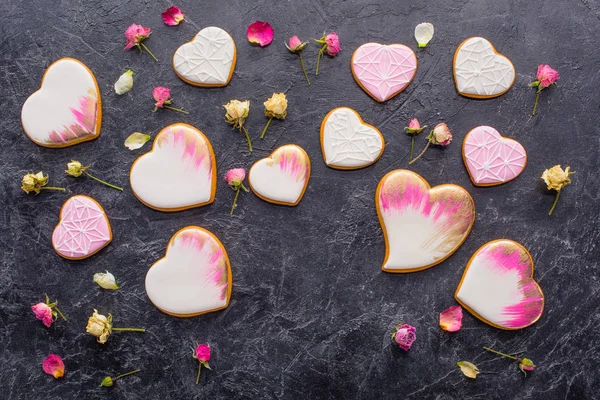 Valentinstag-Arrangement aus glasierten herzförmigen Plätzchen und dekorativen Blumen auf dunkler Tischplatte — Stockfoto
