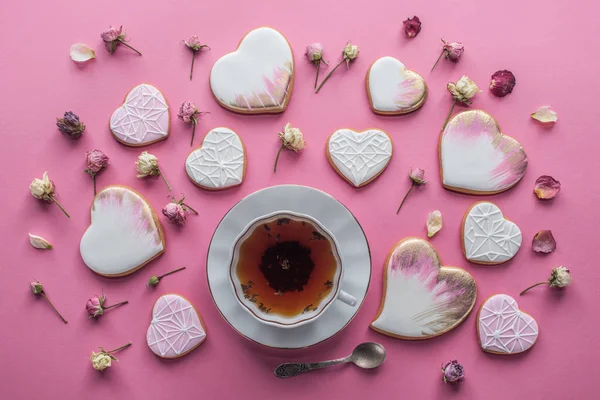 День святого Валентина расположение чашки чая, застекленное печенье в форме сердца и декоративные цветы изолированы на розовый — стоковое фото