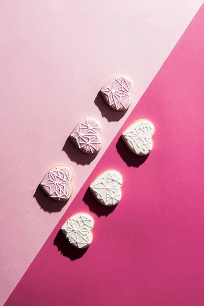 Vista superior de las galletas dispuestas en forma de corazón acristalado en la superficie rosa - foto de stock