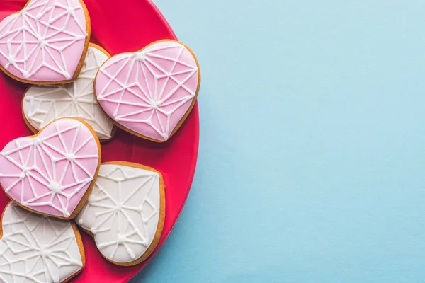 Vista superior de las galletas vidriadas en forma de corazón en placa rosa aislada en azul - foto de stock