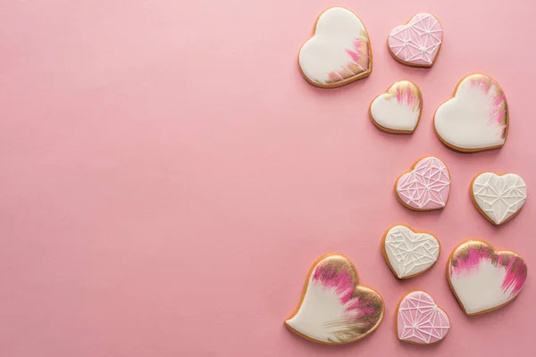 Flache Lage mit Anordnung von glasierten herzförmigen Keksen isoliert auf rosa Oberfläche — Stockfoto