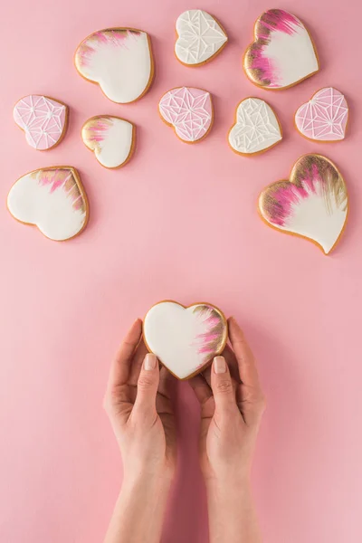 Visão parcial da mulher segurando biscoito vitrificado em mãos isoladas em rosa, st conceito dia dos namorados — Fotografia de Stock