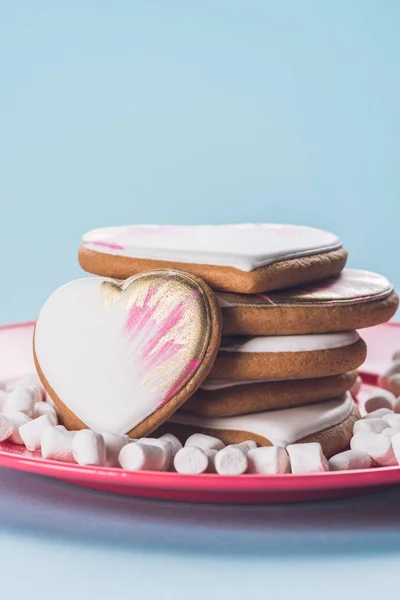 Vista ravvicinata di biscotti smaltati e marshmallow su piastra rosa isolata su blu — Foto stock