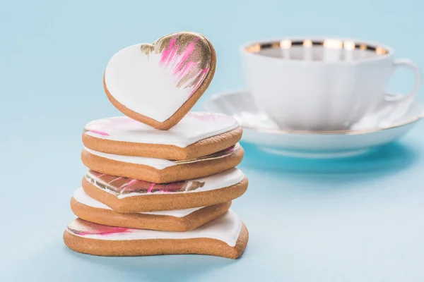 Close up view of pile of glazed heart shaped cookies and cup isolated on blue, st valentines day concept — Stock Photo