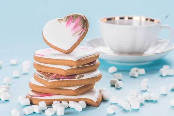 Nahaufnahme von Haufen glasierter herzförmiger Kekse, Marshmallow und Tasse isoliert auf blauem, Valentinstag-Konzept — Stockfoto