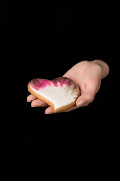 Close up view of female hand with glazed heart shaped cookie isolated on black — Stock Photo