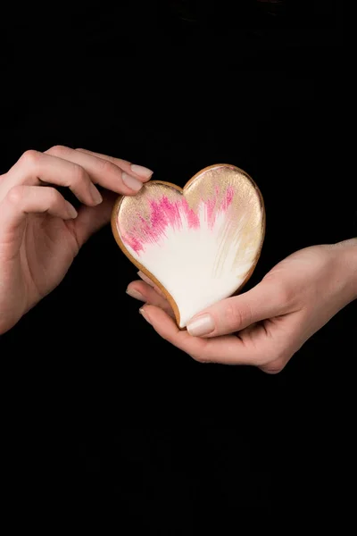 Close up view of female hands with glazed heart shaped cookie isolated on black — Stock Photo