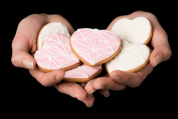 Vista ravvicinata di mani femminili con biscotti a forma di cuore smaltati isolati su nero — Foto stock