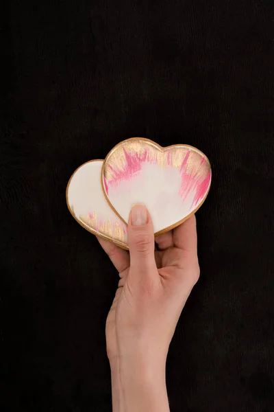 Tiro recortado de mãos femininas segurando biscoitos em forma de coração envidraçado no fundo escuro, st conceito dia dos namorados — Fotografia de Stock