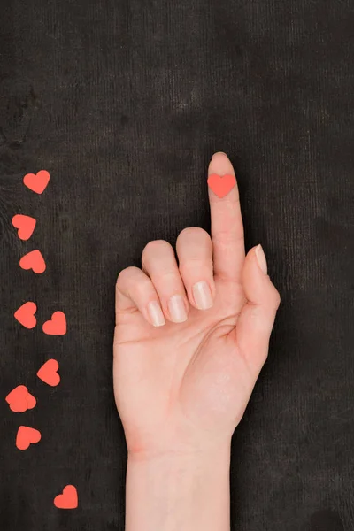 Partial view of female hand and red heart shaped confetti on dark background, st valentines day concept — Stock Photo