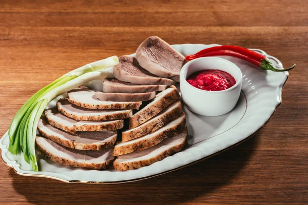 Vista de jamón rebanado en plato blanco con platillo y pimientos rojos en la mesa - foto de stock